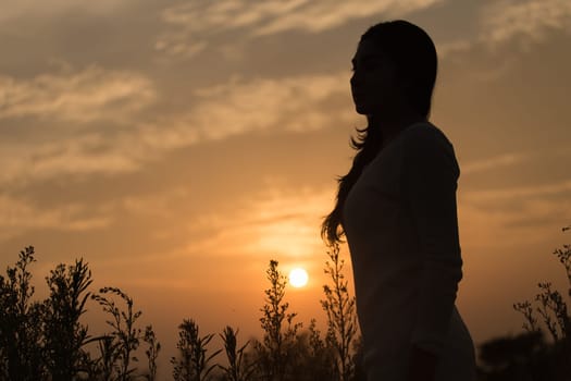 Silhouette of a young asian woman enjoying flowers and nature sunset