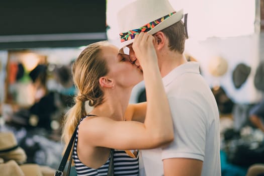 Romantic couple in Queen Victoria Market, Australia. The woman is putting a hat on her partners head and kissing him at the same time.
