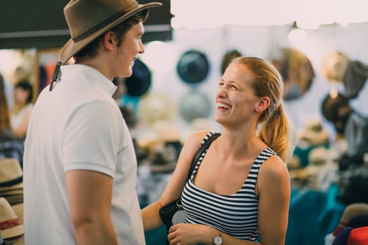 Young couple are exploring Queen Victoria Market in Australia. The woman has put a hat on her boyfriend in a market stall.