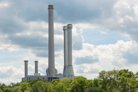 Industrial smokestack over green forest trees against clouds in sky