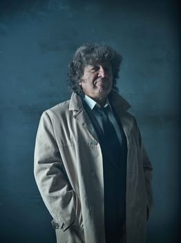 The senior man in cloak as detective or mafia boss. Studio shot on gray in retro stile