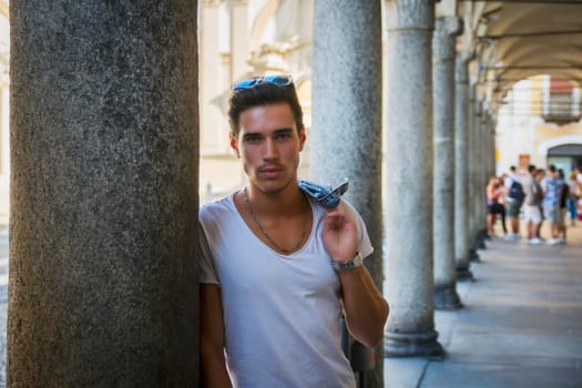 Handsome young man standing outdoors under old colonnade in european town or city