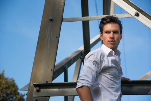 Handsome young man hanging from metal electricity trellis, looking at camera
