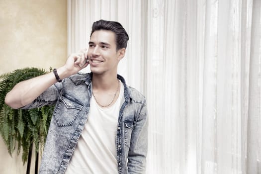 Handsome young man talking on telephone at home, smiling and looking to a side
