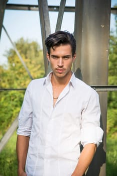Handsome young man leaning against metal electricity trellis, looking at camera