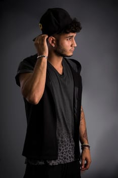 Profile of handsome young man in dark t-shirt and baseball hat, on black background. Looking away