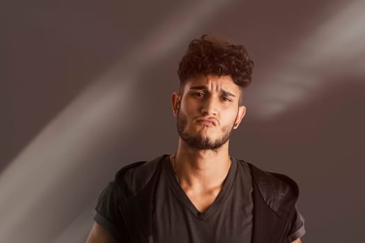 Portrait of handsome young man in dark t-shirt on black background, with an expression of challenge. Looking away
