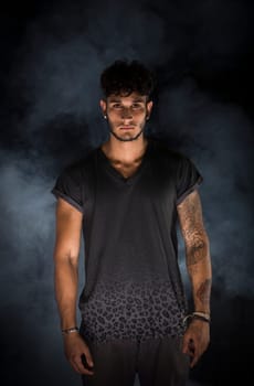 Portrait of handsome young man in dark t-shirt on black background. Dramatic lighting with smoke