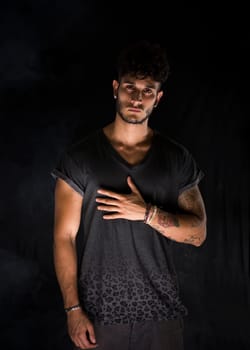 Portrait of handsome young man in dark t-shirt on black background. Dramatic lighting