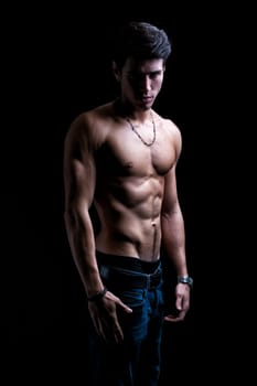 Handsome shirtless muscular young man's profile, looking at camera, on dark background