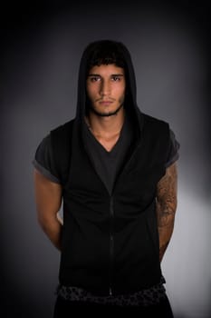 Portrait of handsome young man in dark hoodie on black background. Looking at camera
