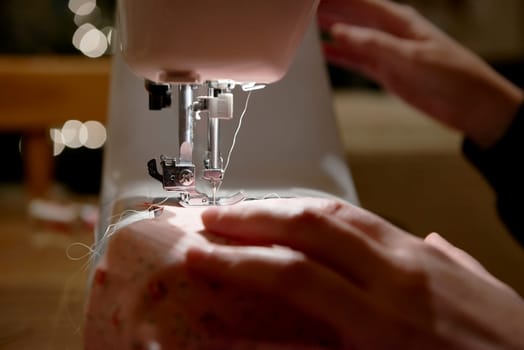 Detail of hands working on piece of fabric on automatic sewing machine, shot from the side