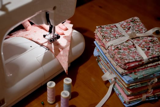 High angle detail of hands working on piece of fabric on automatic sewing machine, with fabric stacked on the side