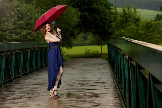 Young attractive woman with red umbrella after rain in nature