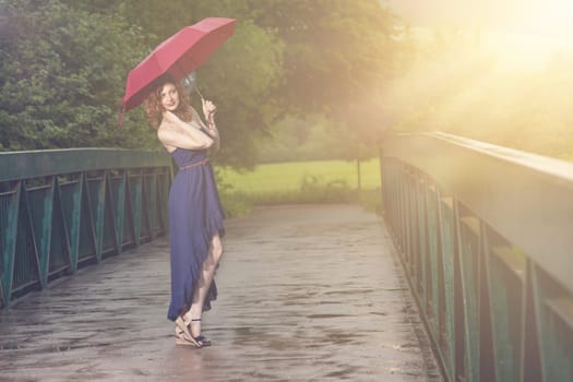 Young attractive woman with red umbrella after rain in nature