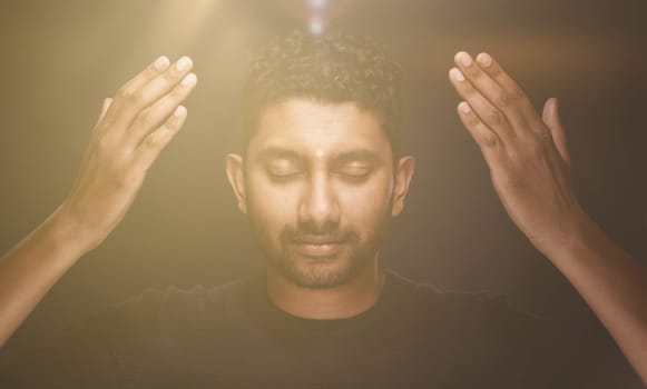 Man meditates or prays and raises hands to the light