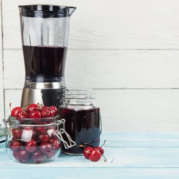 Cherry juice with glass jar,of berries, blender and juice on blue wooden background