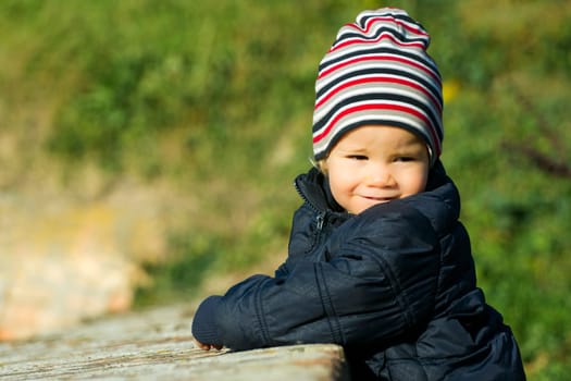Lovely little boy with striped cap is outdoor on green background.
