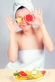 Young woman holds slices of carambola and red grapefruit like her eyes.