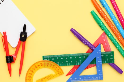 Multicolored pen, rulers and notebook on yellow background