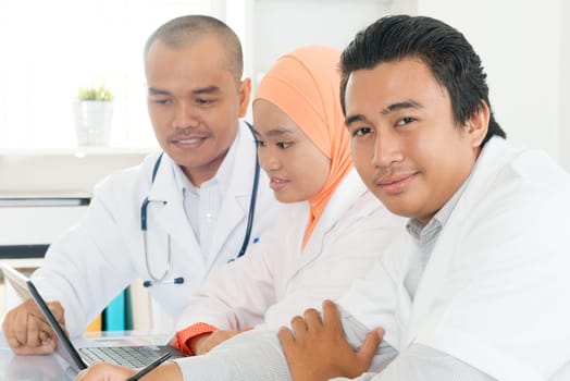 Medical team using a laptop in a bright office. Southeast Asian Muslim doctors and nurses.
