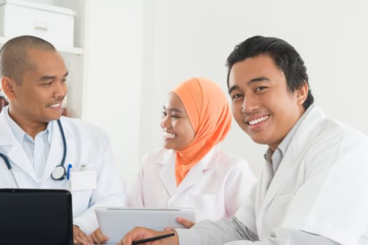 Medical team having discussion on desk inside hospital room. Southeast Asian Muslim doctors and nurses.