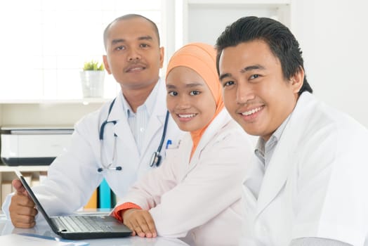 Medical team discuss at meeting in hospital office. Southeast Asian Muslim doctors and nurses.