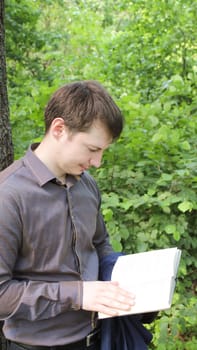 young businessman reading a book in the woods.