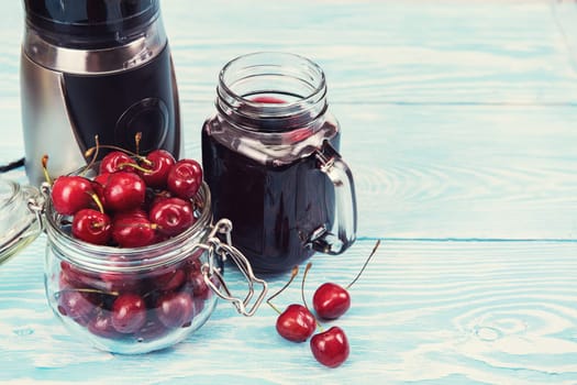 Cherry juice with glass jar,of berries, blender and juice on blue wooden background