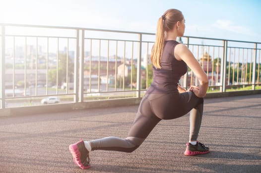 A woman in sportswear doing fitness exercises. City in sunny evening.