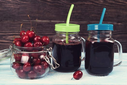 Cherry juice with glass jar of berries on blue wooden background