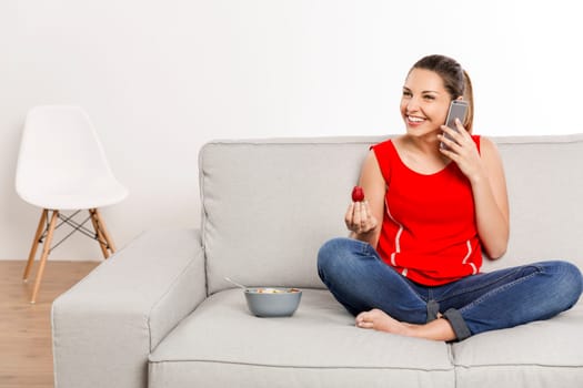 Beautiful happy woman at home making a phone call while eating strawberries