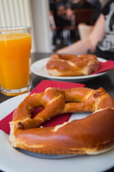 Pretzel bread on white plate and orange juice on wooden table.