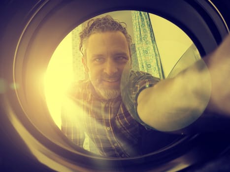 Happy man loading the washing machine, bright sun in the back, golden flat color style