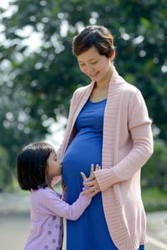 Pregnant mother and her daughter posing on the outdoor when summer
