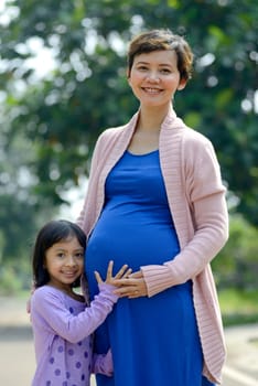 Pregnant mother and her daughter posing on the outdoor when summer