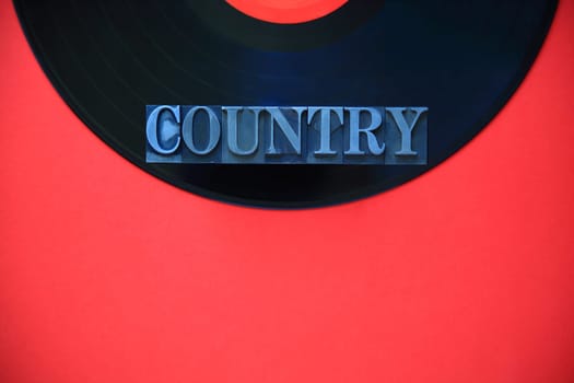 The word country in metal type on a black vinyl record on a red background with copy space