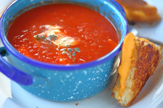 Tomato soup with fresh thyme in an enamelware bowl with a grilled cheese sandwich cut in triangles