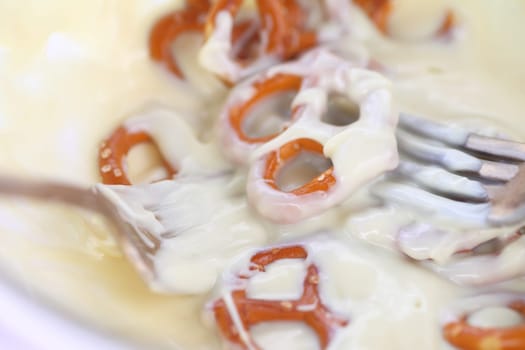 Using two forks to dip small pretzels in melted white chocolate