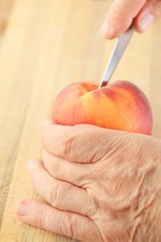 A man cuts into a peach with a paring knife.