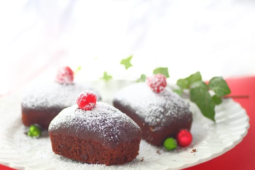 Three miniature chocolate cakes with powdered sugar, fresh raspberries and small Christmas ornaments