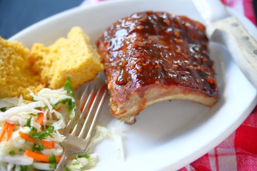 Garlic barbecue sauce on baby back ribs with cornbread and coleslaw on white platter