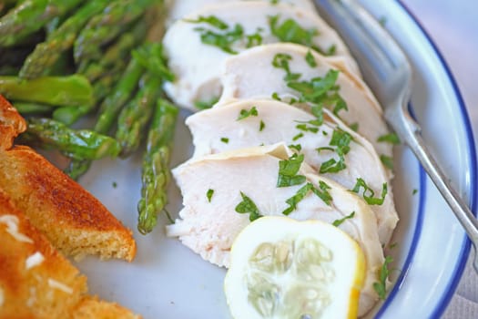 Plate of sliced, poached chicken with garlic bread and sauteed asparagus