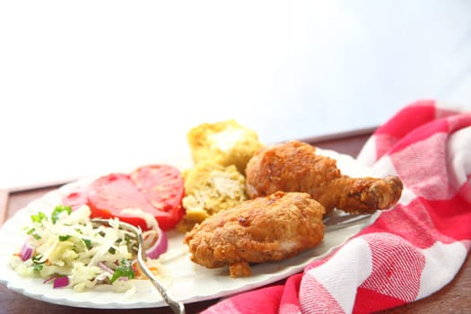 Fried chicken pieces with cornbread, coleslaw and tomato slices with a bright background