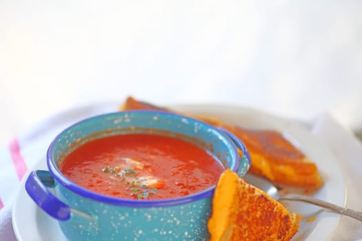 Tomato soup in a blue bowl with a grilled cheese sandwich cut in triangles and room for text