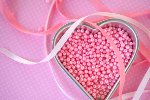 Heart-shaped pan with tiny pink beads used for cake decorating with pink ribbons on a polka dot background