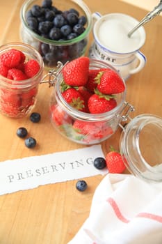 Strawberries, raspberries and blueberries in glass jars with the word preserving on cutting board