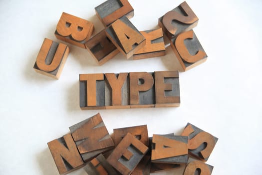 Old letterpress wood letters form the word type on white with other alphabet letters alongside