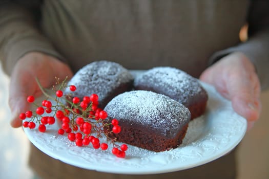 A man holds a decorative plate of miniature chocolate cakes with powdered sugar and red berries
