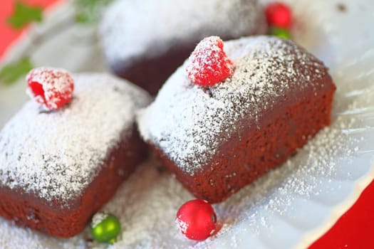 Small chocolate cakes with fresh raspberries and powdered sugar with tiny Christmas ornaments